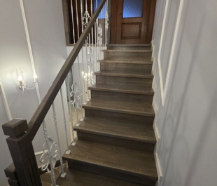 Фото отделки лестницы дубом в Плещеницах: тёмная тонировка, массив на бетонных ступенях, металлические балясины.